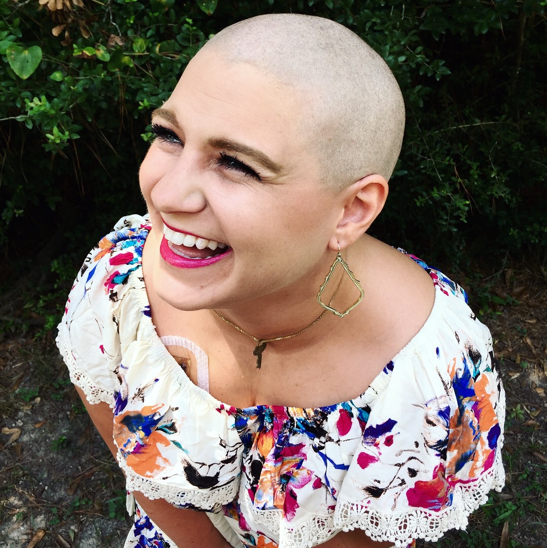 photo of Nicole Body in colorful dress with bright pink lipstick turning to the side laughing and smiling with a bald head showing her joy through cancer.