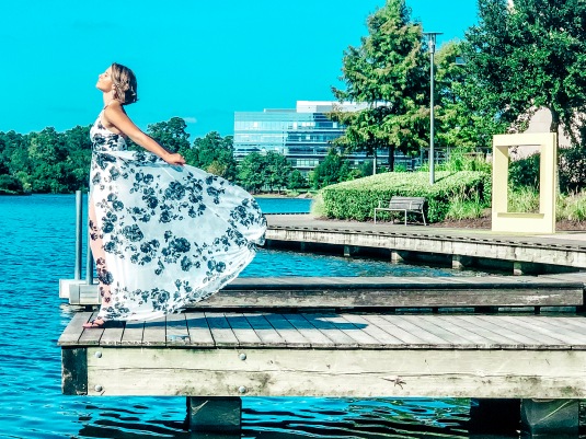 Nicole on a dock at Lake Woodlands staring out into the water with her dress fanned back.